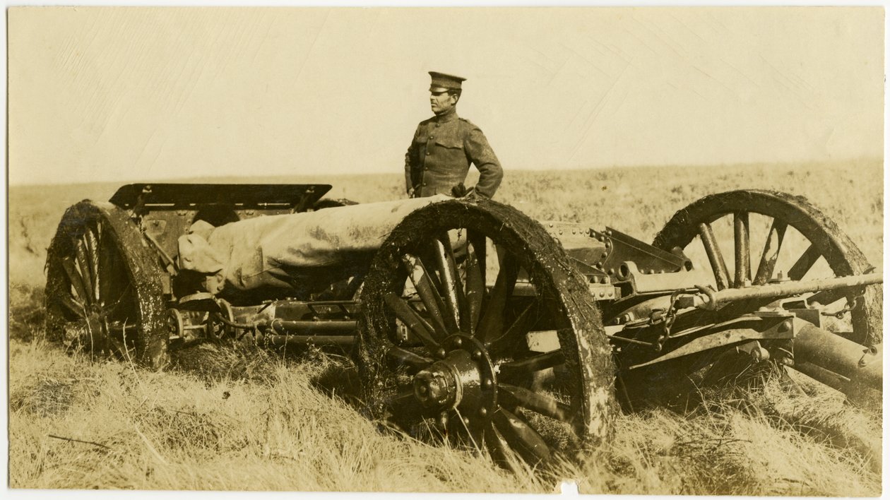 Fotografía horizontal en sepia que muestra a un hombre uniformado junto a un cañón de artillería sobre ruedas en un campo abierto de Carl Michel