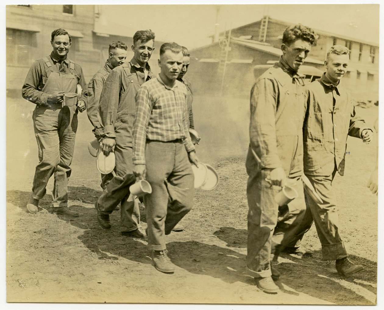 Siete hombres caminando por un camino de tierra con kits de comida y tazas de Carl Michel