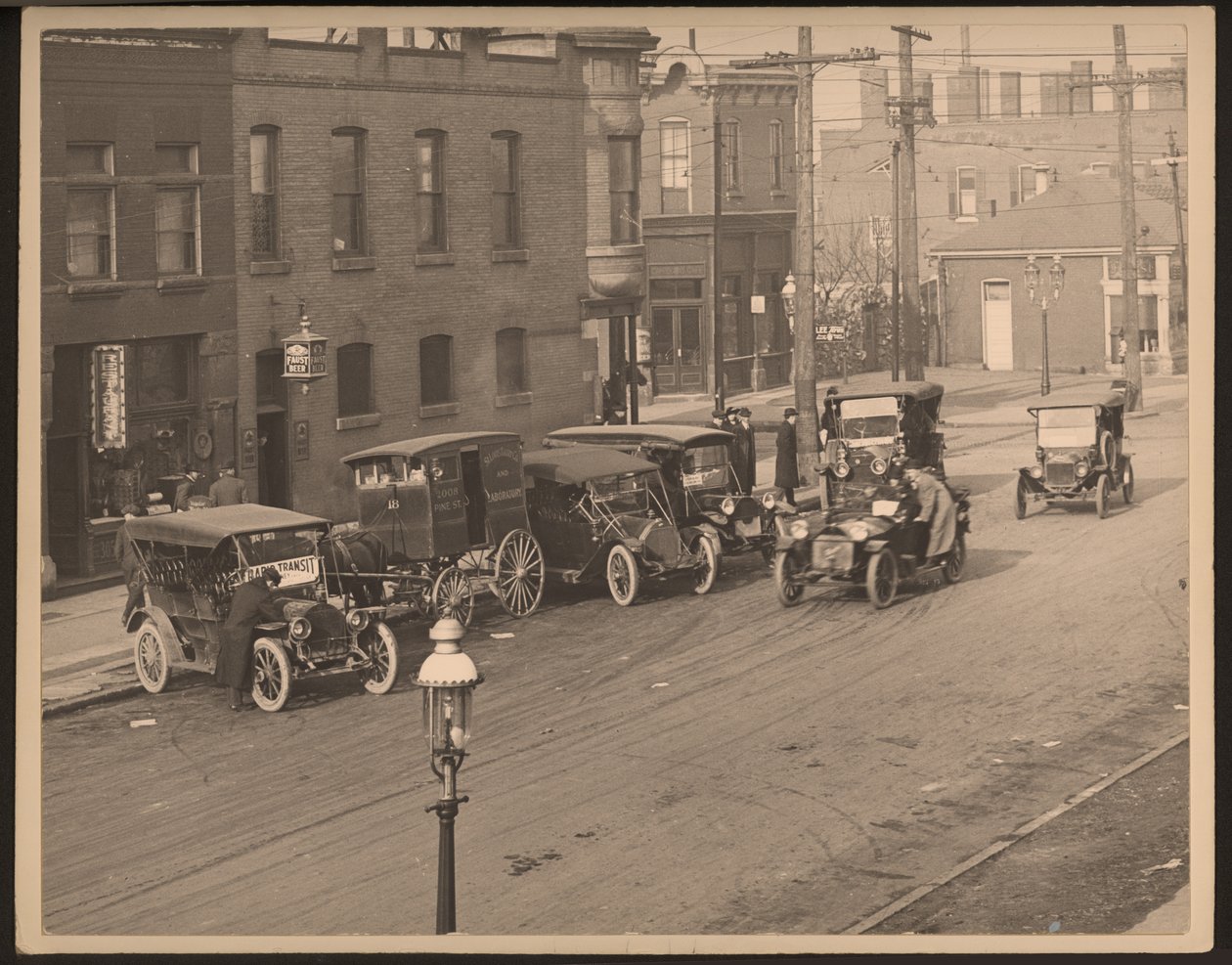 Vista de una calle no identificada con varios automóviles y un carro de reparto tirado por caballos de la St. Louis Bakery Company estacionado en la acera de William G. Swekosky